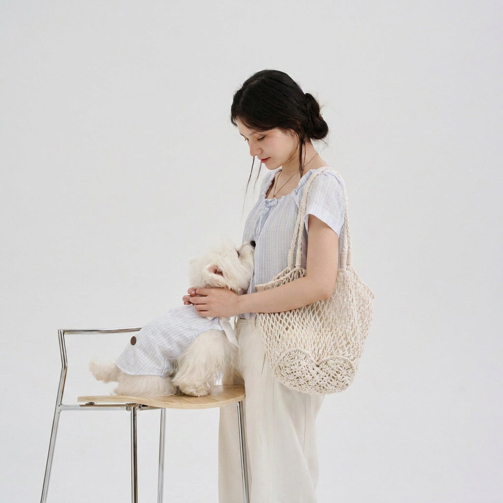 Pet parent wearing a light blue striped top while gently interacting with a white small dog in a matching striped dog shirt, featuring soft dog apparel and a coordinated pet parent outfit.