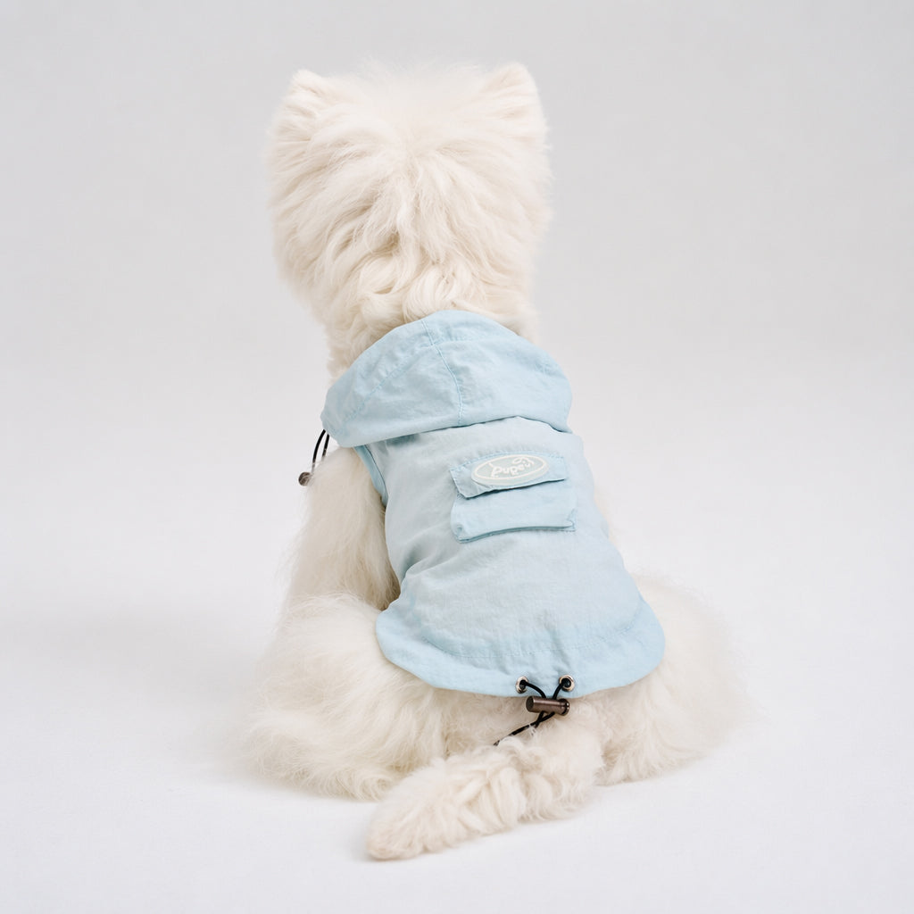White small dog shown from the back wearing a light blue hooded dog sun jacket with a back pocket and adjustable hem, featuring lightweight dog apparel for warm-weather outdoor wear.