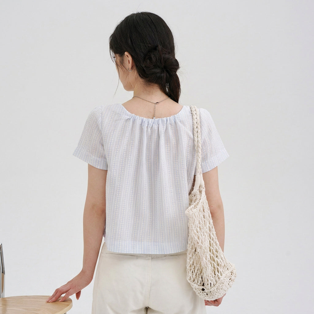 Back view of a woman wearing a light blue striped pet parent blouse with short sleeves and a relaxed cropped fit, designed as the owner piece for a matching pet and owner outfit collection.
