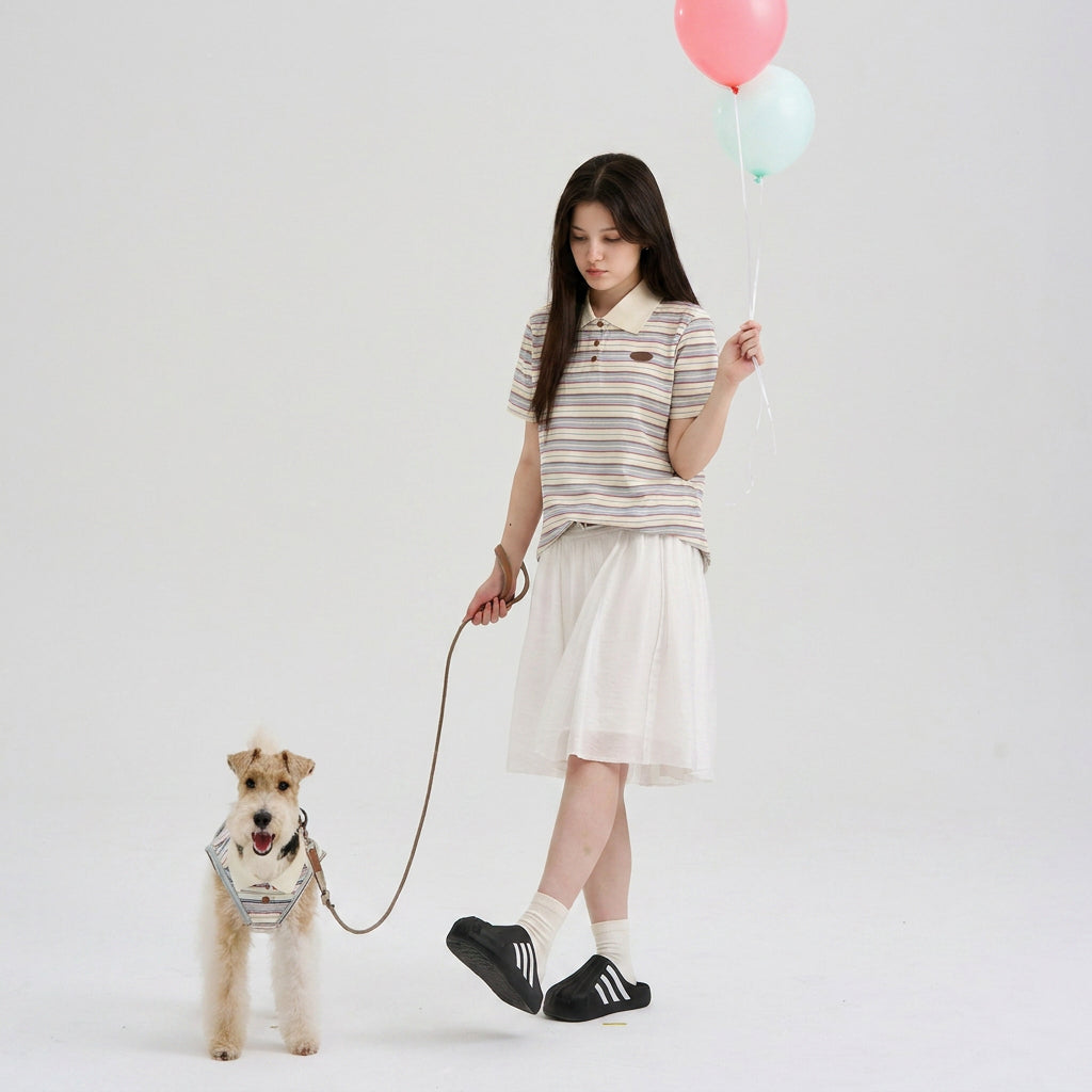 Pet parent wearing a striped polo and holding balloons while walking a small terrier in a coordinated striped dog polo, featuring casual dog apparel and matching dog and owner clothes for playful outings.