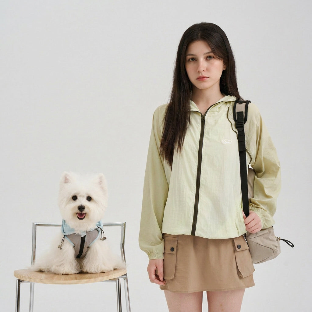 Pet parent wearing a pale green sun protection jacket beside a white small dog in a light blue sun protection dog jacket, featuring lightweight dog apparel and a coordinated pet parent matching outfit.
