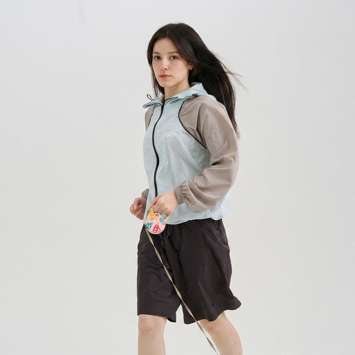 Female model wearing a light blue and gray hooded sun protection jacket with black shorts.