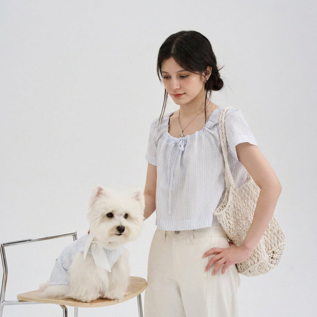Pet parent wearing a light blue striped top with a white small dog in a matching light blue striped dog shirt, featuring soft dog apparel and a cute pet parent matching outfit for everyday style.