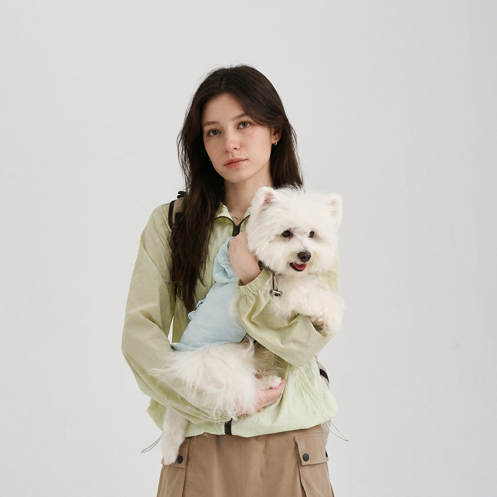 Pet parent wearing a light green hooded sun protection jacket while holding a white small dog in a light blue dog hoodie, featuring a casual matching dog and owner outfit for everyday moments.