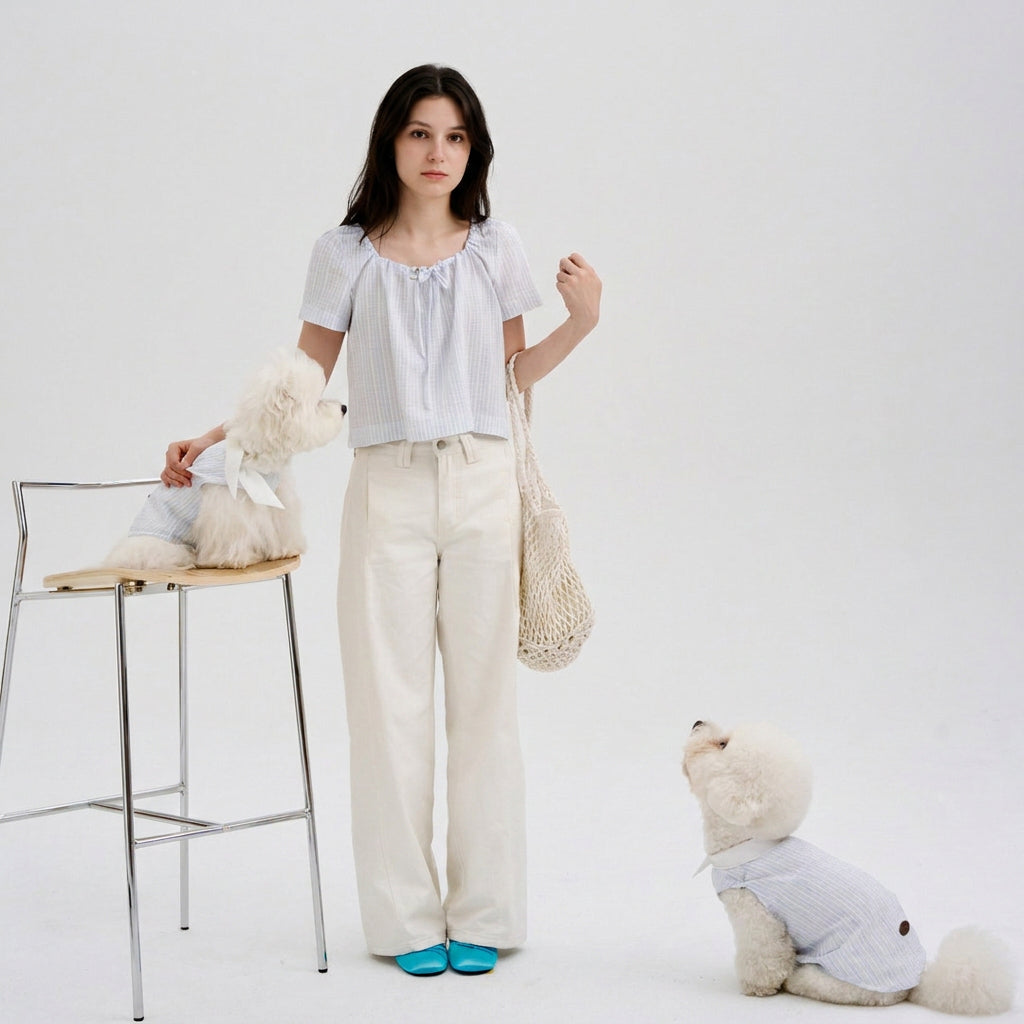 Woman wearing a light blue striped blouse standing with two white small dogs in matching blue striped dog shirts, featuring soft dog apparel and pet parent matching clothes.