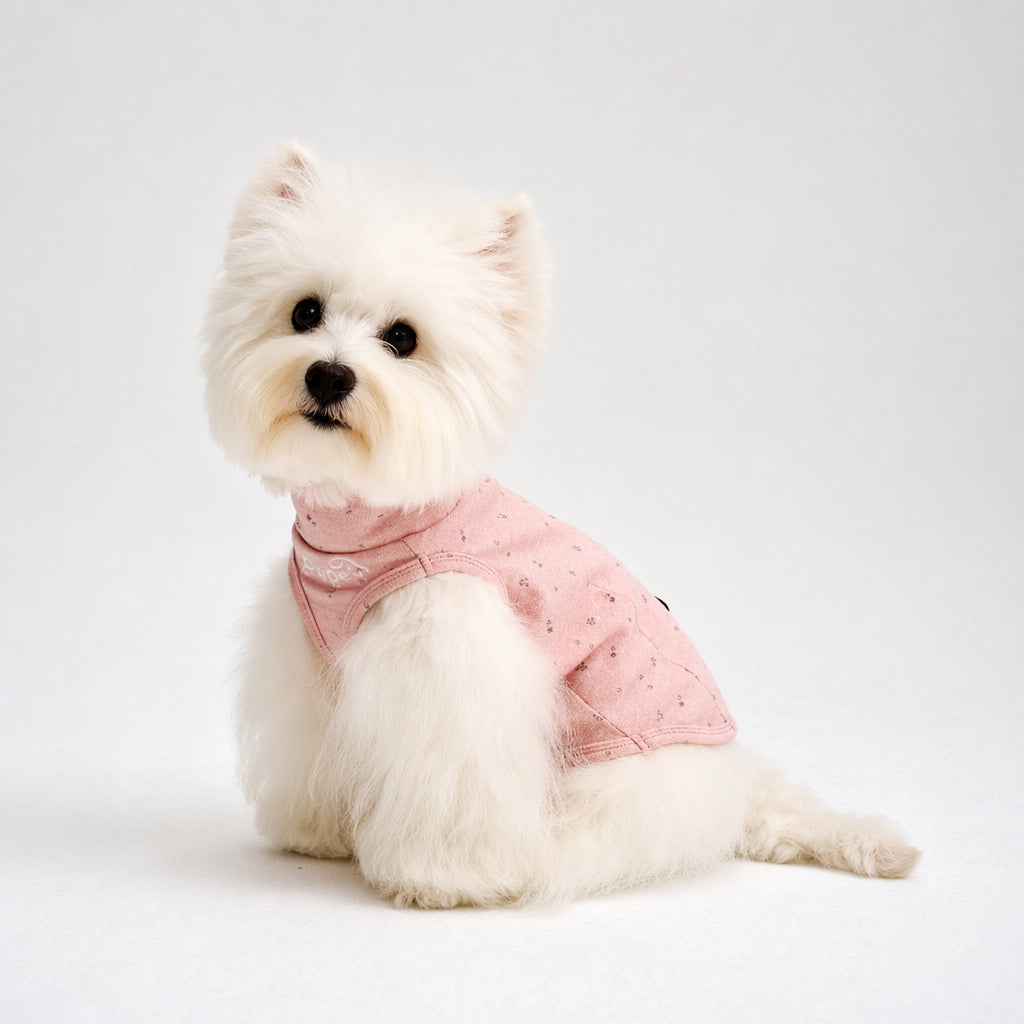 White small dog sitting in a pink speckled dog shirt, featuring soft dog apparel and comfortable small dog clothes for cute everyday pet clothing style.