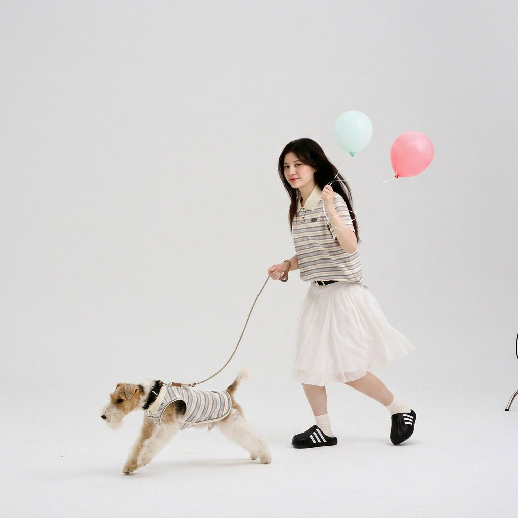 Pet parent in a striped polo holding pastel balloons while walking a small terrier in a matching striped dog polo, featuring casual dog apparel and playful matching dog and owner clothes.
