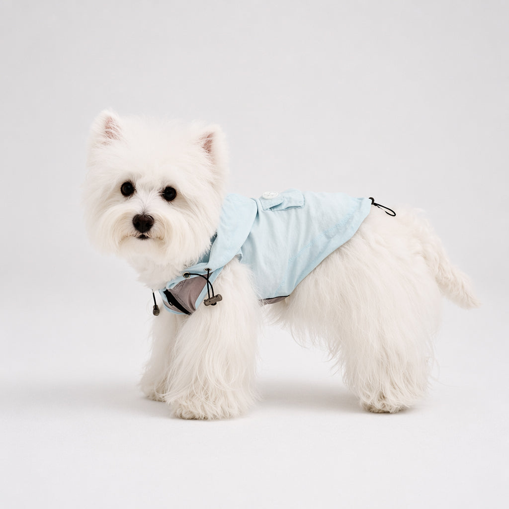 White small dog shown in side profile wearing a light blue hooded dog sun protection jacket with a back pocket and adjustable hem, featuring lightweight dog apparel for outdoor comfort.