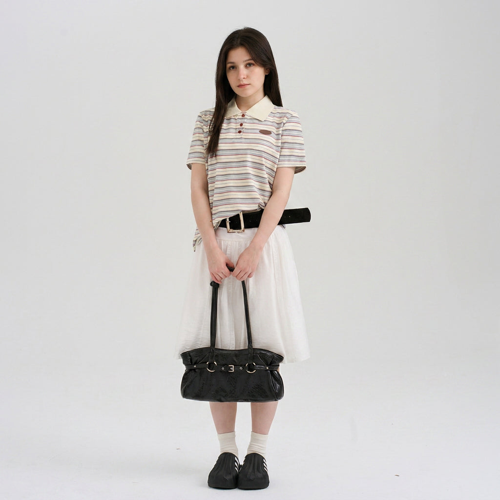 Woman wearing a striped short sleeve polo shirt and white skirt while holding a black handbag in a clean setting.